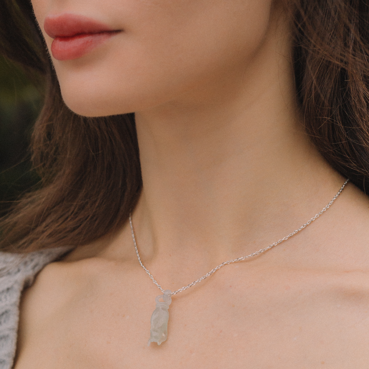 Close-up of a woman wearing a delicate silver necklace with a leaf pendant.